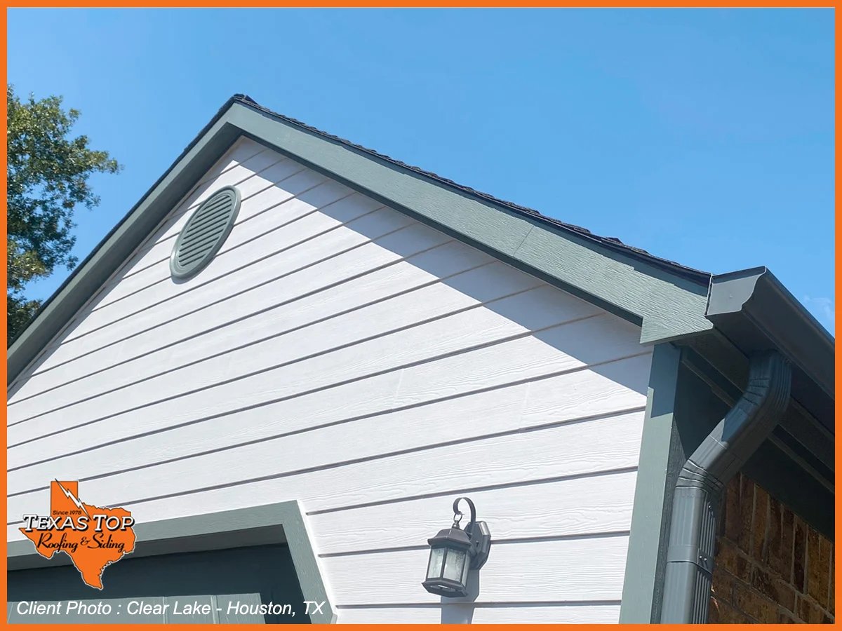 White residential garage with gabled roof, dark trim, and hanging lantern against clear blue sky