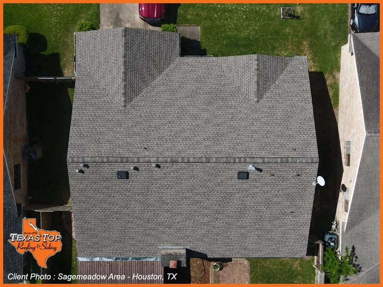 Aerial view of a gray shingled residential roof with surrounding green lawn and driveway